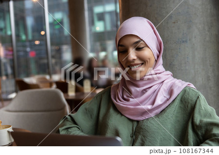 Cute woman in hijab sitting in a cafe and smiling 108167344