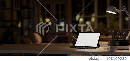 A digital tablet white-screen mockup on a desk in a modern dark room at night. Home workspace 108169229