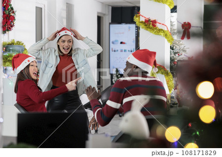 Coworkers having fun in festive decorated office, making fun of each other at work during winter holiday season. Employees laughing together in Christmas ornate workspace 108171829