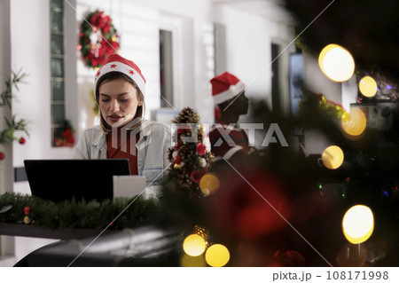 Businesswoman in festive decorated workspace working hard on computer tasks for upcoming project. Employee researches company startup plans during Christmas holiday season 108171998