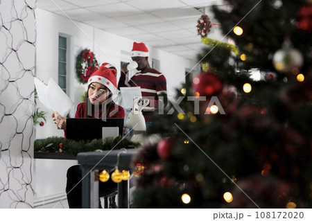 Tired asian employee crosschecking company paperwork in Christmas decorated office. Stressed businesswoman struggling to finish project on time in festive adorn workspace Tired asian employee crosschecking company paperwork in Christmas decorated office. Stressed businesswoman struggling to finish project on time in festive adorn workspace 108172020