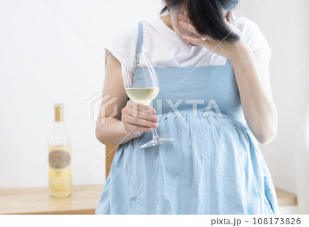 ワインボトルと頭を抱えている妊婦がグラスワインを持っているイメージ ワインボトルと頭を抱えている妊婦がグラスワインを持っているイメージ 108173826
