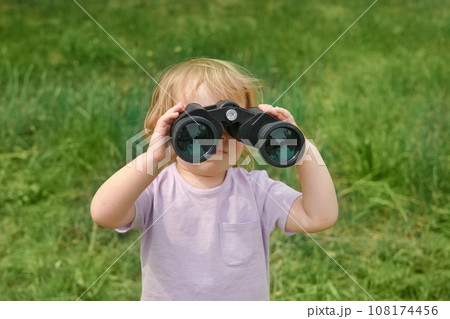 Little girl using binoculars in a forest. 2 years kid looking ahead. Smiling baby with spyglass. Adventure, Imagination, travel concept. Freedom, vacation. Happy child playing outdoor in summer field 108174456