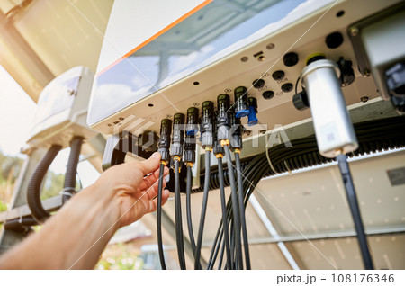 Professional worker connecting wires to solar inverter. Pov of configuring inverter. Male worker turning on PV battery. 108176346