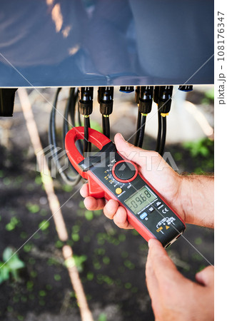 Checking of output voltage level of inverter. Professional worker using current clamps to measure voltage. Techinician service of phototvoltaic battery. Checking of output voltage level of inverter. Professional worker using current clamps to measure voltage. Techinician service of phototvoltaic battery. 108176347