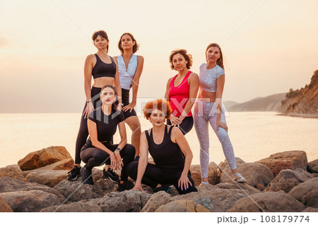 Group of multiethnic beautiful women wearing sportswear posing at rocks. Sea and sunset in background. Concept of sport and team spirit 108179774