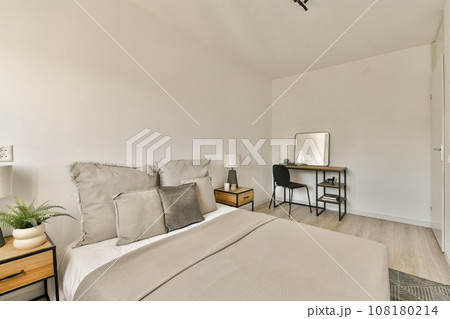 a bedroom with a bed, desk and mirror on the wall next to the bed is a small wooden table a bedroom with a bed, desk and mirror on the wall next to the bed is a small wooden table 108180214