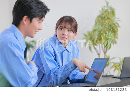 PCを見ながら打ち合わせる作業着の男女1 PCを見ながら打ち合わせる作業着の男女1 108181228
