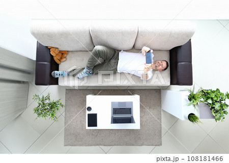 Man lie on sofa and hold modern smartphone in hand 108181466