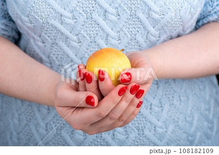 An apple in the hands of a young woman in a blue jumper. An apple in the hands of a young woman in a blue jumper. 108182109