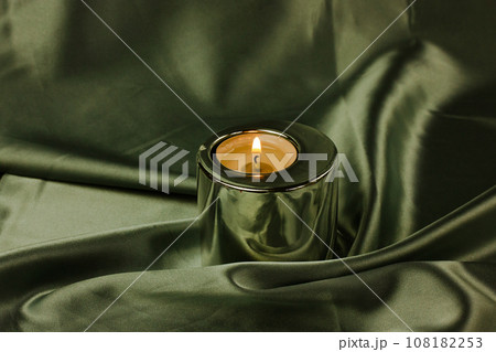 A candle in a metal holder on a dark olive green silk tablecloth. Stylish decor. A candle in a metal holder on a dark olive green silk tablecloth. Stylish decor. 108182253