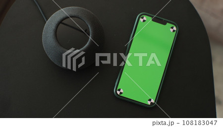 HomePod Mini speaker - the smart speaker on the table and smartphone with green screen. Concept of a smart home. HomePod Mini speaker - the smart speaker on the table and smartphone with green screen. Concept of a smart home. 108183047