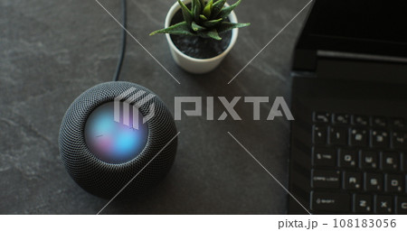 Using an HomePod Mini speaker - the smart speaker is reacting to voice listening to human commands and signalling its attention by the changing lights. Concept of a smart home. Using an HomePod Mini speaker - the smart speaker is reacting to voice listening to human commands and signalling its attention by the changing lights. Concept of a smart home. 108183056