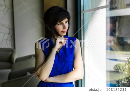 Girl in a blue dress near the window with bright sunlight Girl in a blue dress near the window with bright sunlight 108183251