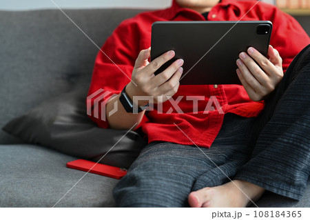 Relaxed young man sitting on couch and browsing internet or watching social media videos on digital tablet Relaxed young man sitting on couch and browsing internet or watching social media videos on digital tablet 108184365