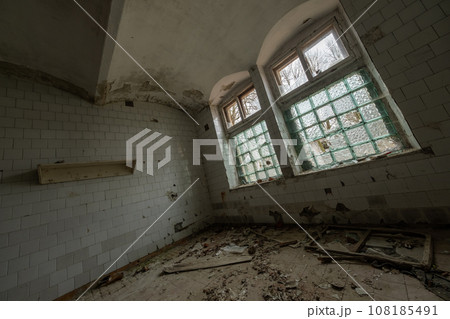 Low angle of interior of abandoned spacious hall with stone brick wall arched glass windows and rubbish trash furniture waste strewn on uncleaned floor in daylight Low angle of interior of abandoned spacious hall with stone brick wall arched glass windows and rubbish trash furniture waste strewn on uncleaned floor in daylight 108185491