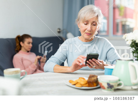 Young woman and her grandmother with smartphones at home 108186387
