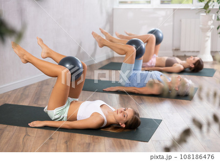 Family grandmother, mother and granddaughter perform fitness exercises lying on floor with softball. Family grandmother, mother and granddaughter perform fitness exercises lying on floor with softball. 108186476