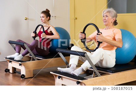 Elderly woman exercising with flex ring and fitball on pilates reformer Elderly woman exercising with flex ring and fitball on pilates reformer 108187015
