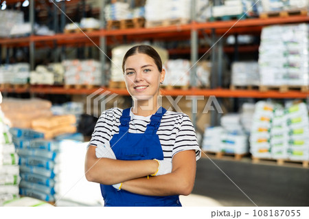 Positive warehouse girl employee stands with arms crossed over chest. Positive warehouse girl employee stands with arms crossed over chest. 108187055