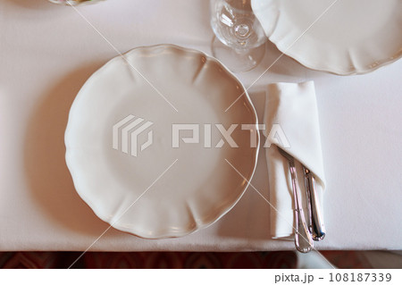 Porcelain white plate, glass and cutlery in napkin on table. Porcelain white plate, glass and cutlery in napkin on table. 108187339