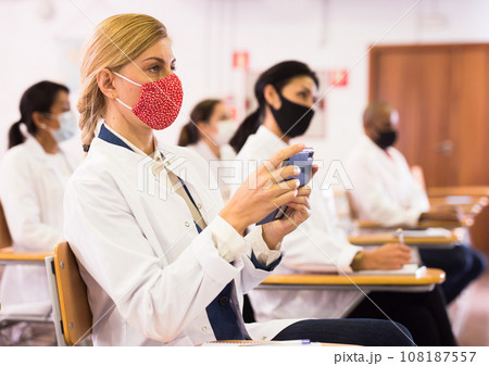Woman in protective mask recording lecture on smartphone at medical seminar 108187557