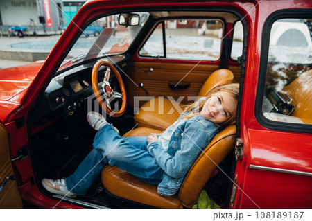 Teenage girl in denim clothes driving a red vintage retro car . 108189187