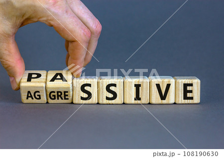 Hand turns cubes and changes the word 'passive' to 'aggressive', or vice versa. Business and psychological concept. Beautiful grey background, copy space. Hand turns cubes and changes the word 'passive' to 'aggressive', or vice versa. Business and psychological concept. Beautiful grey background, copy space. 108190630