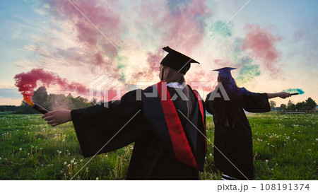 Students graduate with colored smoke walking through the meadow in the evening. 108191374