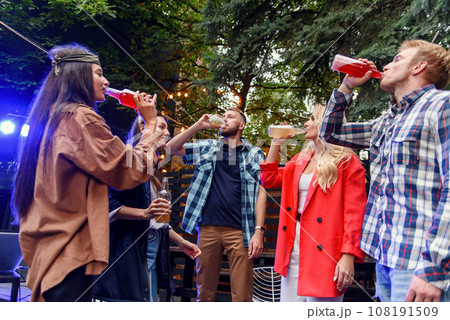 Group of young friends having fun at a poolside summertime party, drinking beer and inviting more friends to join them 108191509
