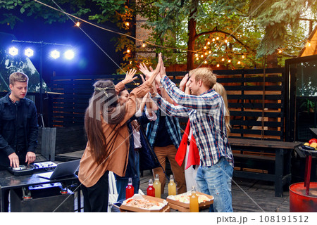 Group of young caucasian friends giving high five together and celebrating party in house courtyard at the evening. 108191512