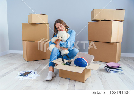 Beautiful smiling girl puts on the headphones on the teddy bear toy and sitting on the floor in the empty new apartment. Beautiful smiling girl puts on the headphones on the teddy bear toy and sitting on the floor in the empty new apartment. 108191680