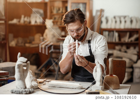 Male potter looking to the handmade cap during work day in the pottery. Male potter looking to the handmade cap during work day in the pottery. 108192610