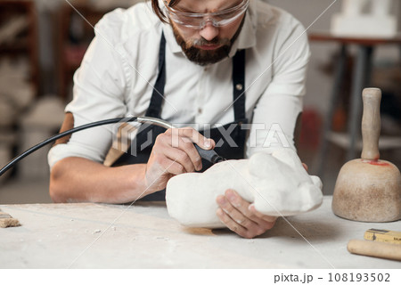 Attentive stonemason with stylish beard in protective goggles detailing creative sculpture of woman torso at his workplace. Attentive stonemason with stylish beard in protective goggles detailing creative sculpture of woman torso at his workplace. 108193502