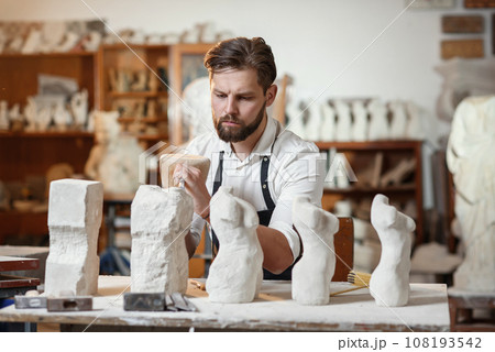 Male craftsman in working uniform makes a limestone copy of woman torso at the creative studio and show making process from start to finish. Male craftsman in working uniform makes a limestone copy of woman torso at the creative studio and show making process from start to finish. 108193542