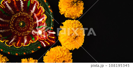 Diwali's radiance shines through, A stunning Diwali lamp and intricate flower rangoli on a captivating black backdrop. Perfect for festive invitations and religious ceremonies. 108195345