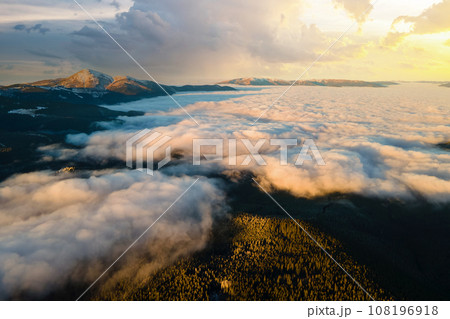Aerial view of vibrant sunrise over white dense clouds with distant dark mountains on horizon. 108196918