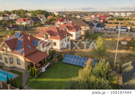 Aerial view of a residential private house with solar panels on roof and wind generator turbine. 108197484