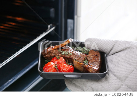 Chef taking delicious roasted ribs out of oven, closeup Chef taking delicious roasted ribs out of oven, closeup 108204439