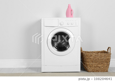 Modern washing machine with detergent and laundry basket near white wall Modern washing machine with detergent and laundry basket near white wall 108204641