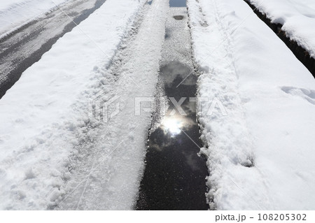 雪道のわだちの雪が溶けた水溜りに映った太陽 108205302