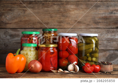 Glass jars with different pickled vegetables on wooden table 108205850