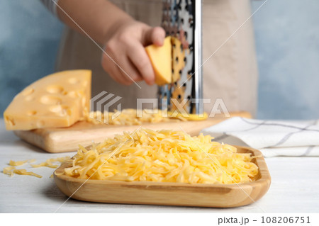 Woman grating cheese at table, focus on wooden plate 108206751