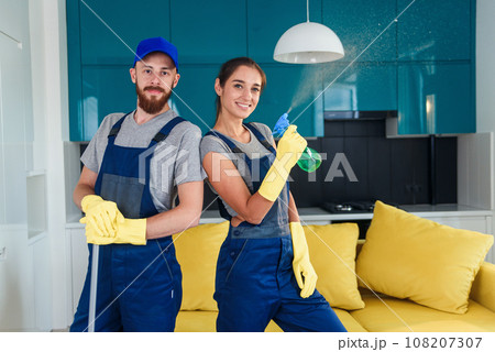 Couple of professional cleaners stay together in the contemporary cuisine with detergents. House cleaning services concept. Couple of professional cleaners stay together in the contemporary cuisine with detergents. House cleaning services concept. 108207307
