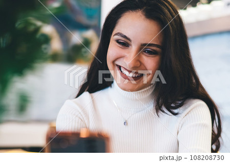 Cheerful female watching smartphone in cafe Cheerful female watching smartphone in cafe 108208730