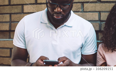 Half length portrait of curly hipster girl dressed in casual wear holding cellular gadget in hands 108209151