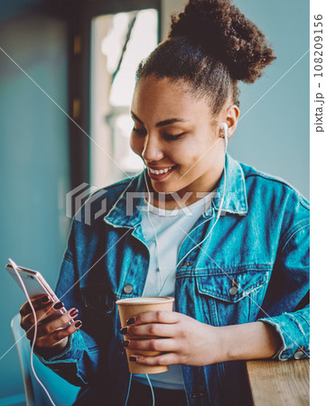 smiling black hipster girl messaging via cellular 108209156