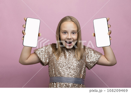 Happy surprised child with two phone. Little girl holding smartphone with blank empty white screen  108209469