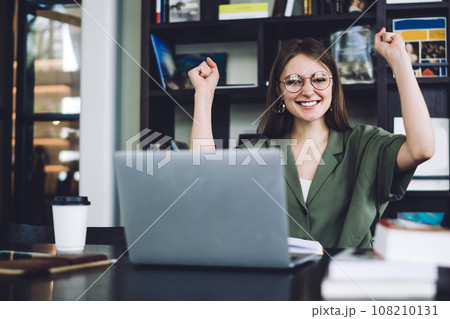 Excited female student sitting with and raising fists Excited female student sitting with and raising fists 108210131