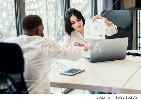 Likable purposeful business partners carefully studying financial documents with charts at the boardroom table at the meeting room. Likable purposeful business partners carefully studying financial documents with charts at the boardroom table at the meeting room. 108210285